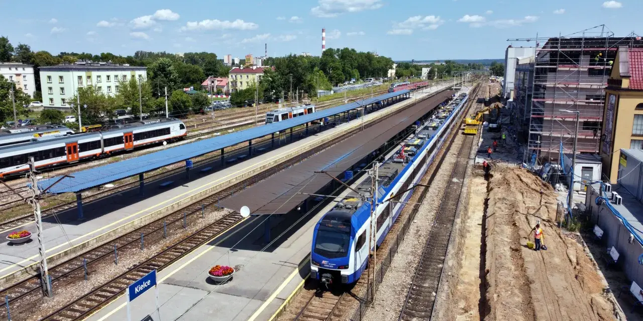 Widok z góry na dworzec kolejowy w Kielcach z pociągami na torach i placem budowy.