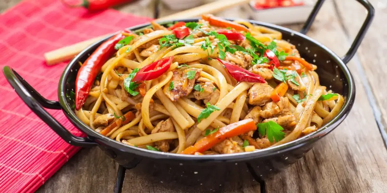 Pyszny makaron chain main z kurczakiem, papryką i chili, posypany natką pietruszki, w czarnej woku.