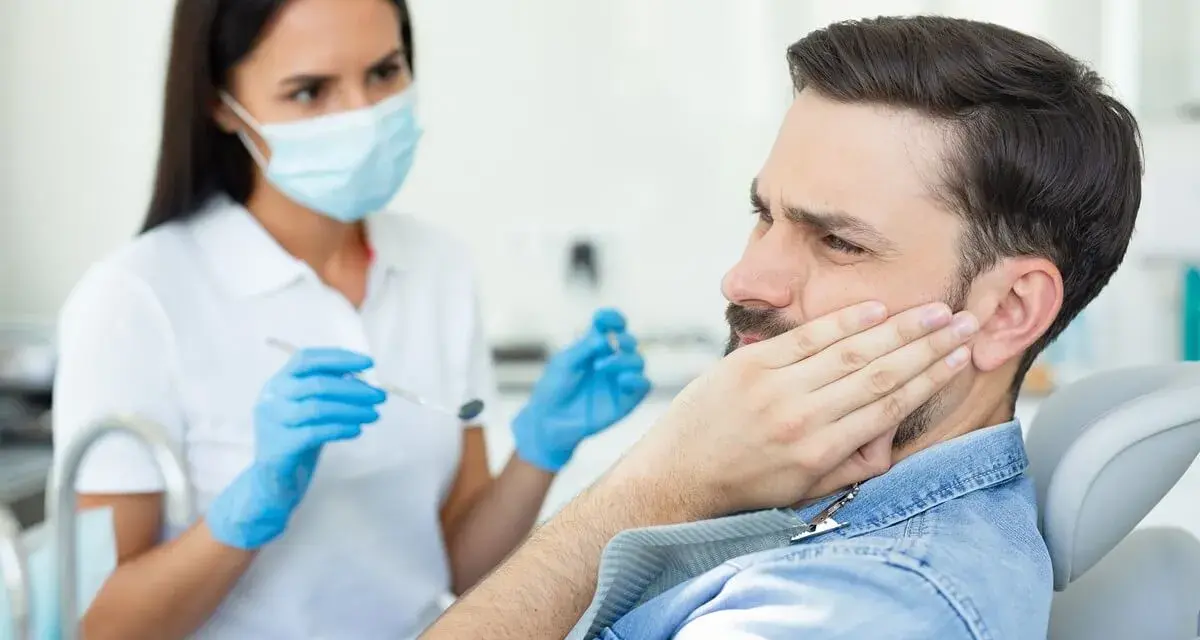 Mężczyzna z bólem policzka u dentysty, który bada jego dziąsła. Może to być objaw problemów z kieszonkami dziąsłowymi.