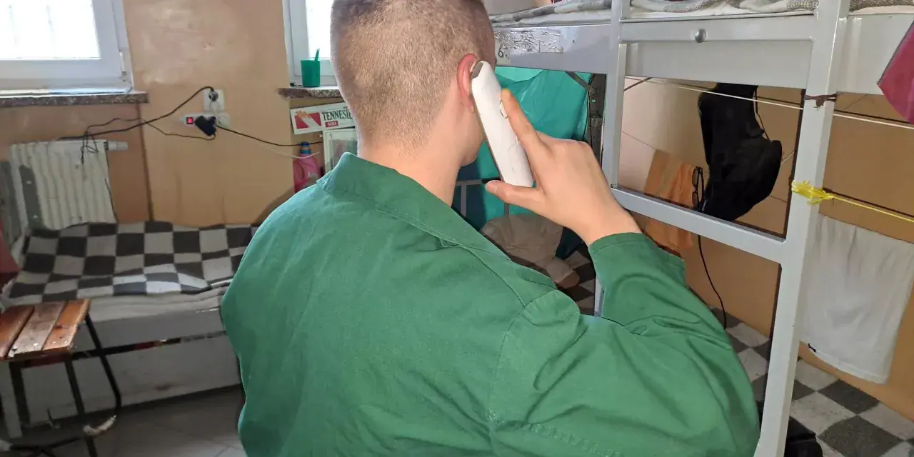 Mężczyzna w zielonym uniformie rozmawia przez telefon. Czeka na odpowiedni moment, po jakim czasie więzień może dzwonić do rodziny.