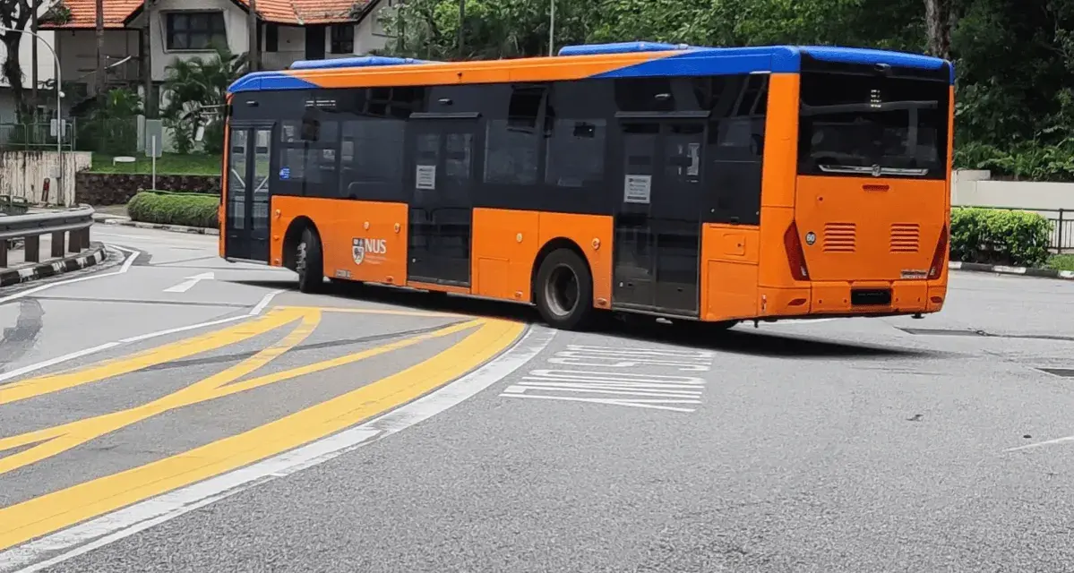 Pomarańczowo-niebieski autobus miejski na zakręcie drogi z żółtymi pasami.