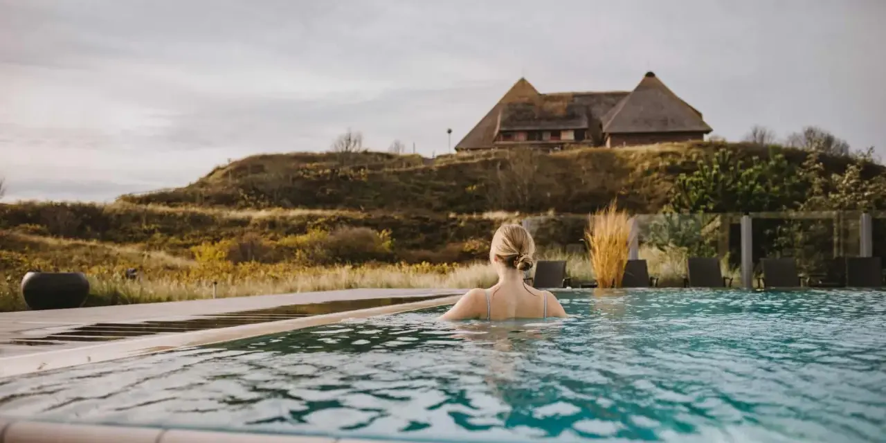 Frau genießt entspannten Wellness Tag in Schleswig-Holstein. Ein idyllischer Pool mit Blick auf Reetdachhaus und Dünenlandschaft.