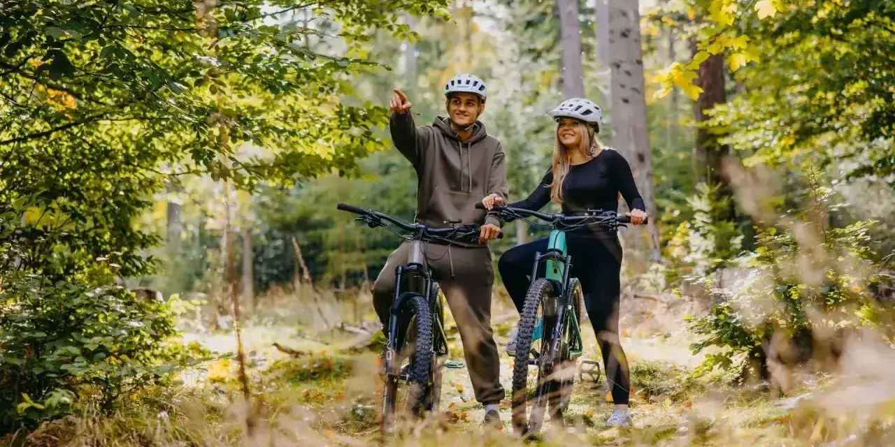 Para rowerzystów w kaskach na leśnej ścieżce. Mężczyzna wskazuje drogę, odkrywając piękną trasę w Szklarskiej Porębie.