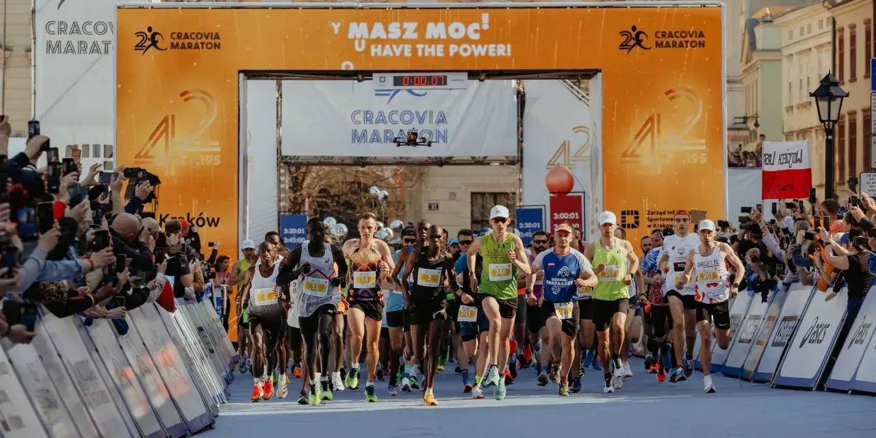 Zawodnicy przekraczają linię startu Maratonu Cracovia. Tłum kibiców z telefonami dokumentuje to wydarzenie.