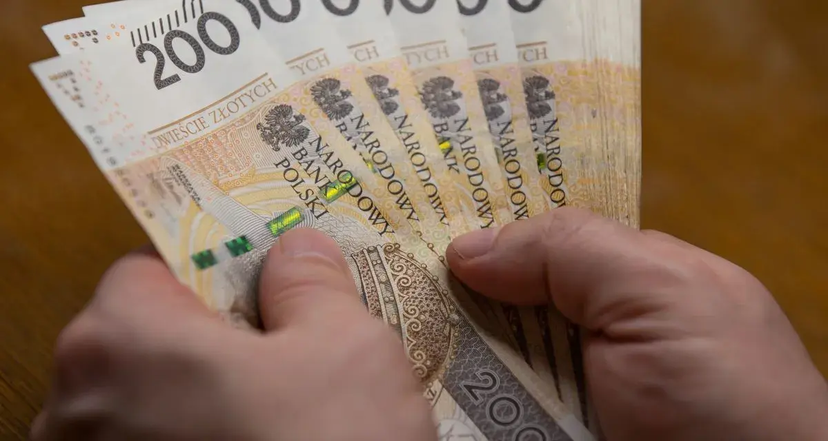 Dłonie trzymają stos banknotów po 200 zł. Czy to wystarczy, by poznać, ile wynosi najniższa krajowa netto?