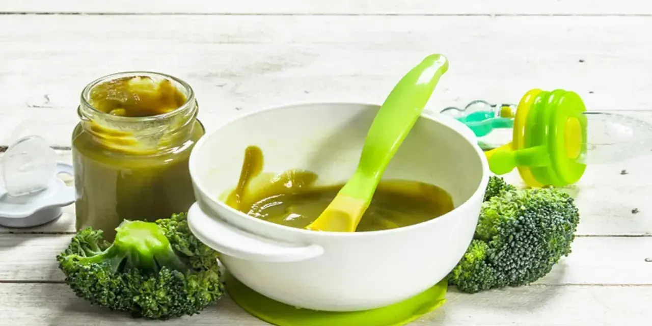Babybrokkoli-Püree im Glas und Schüssel, daneben frischer Brokkoli und ein Löffel.