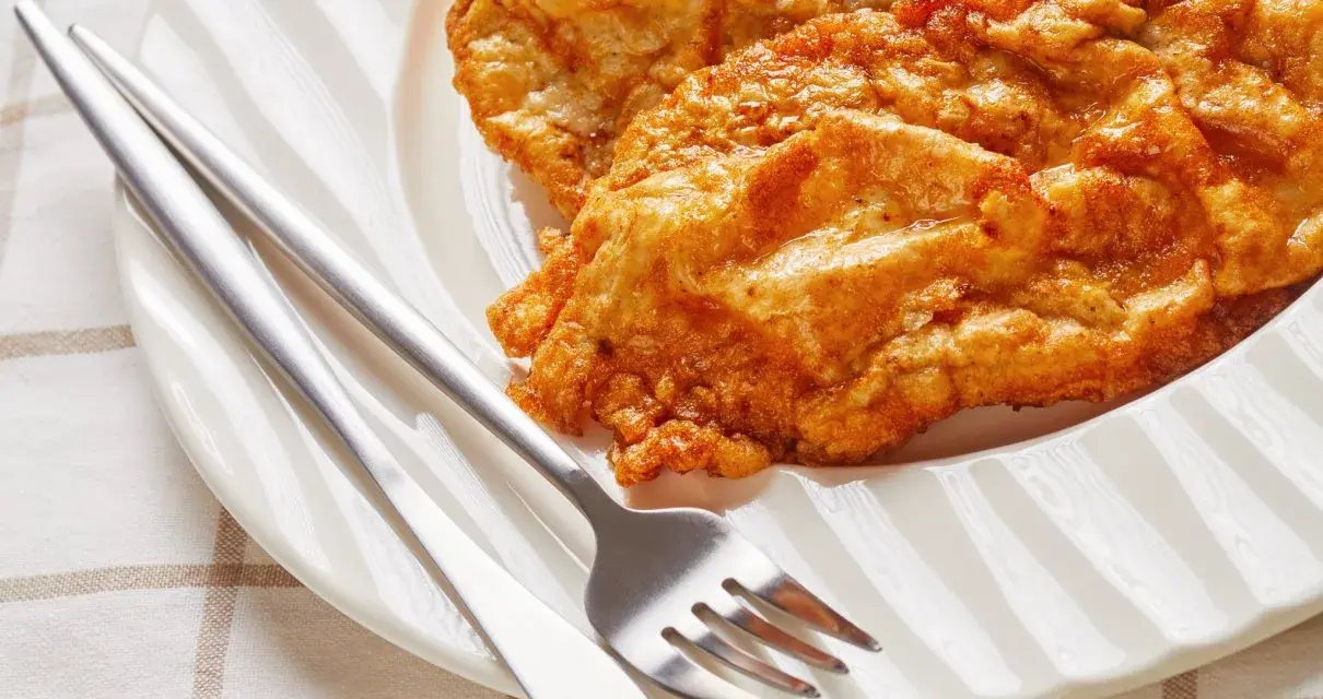 Złocisty kotlet słoneczny na białym talerzu, obok sztućce. Idealny na słoneczny dzień.