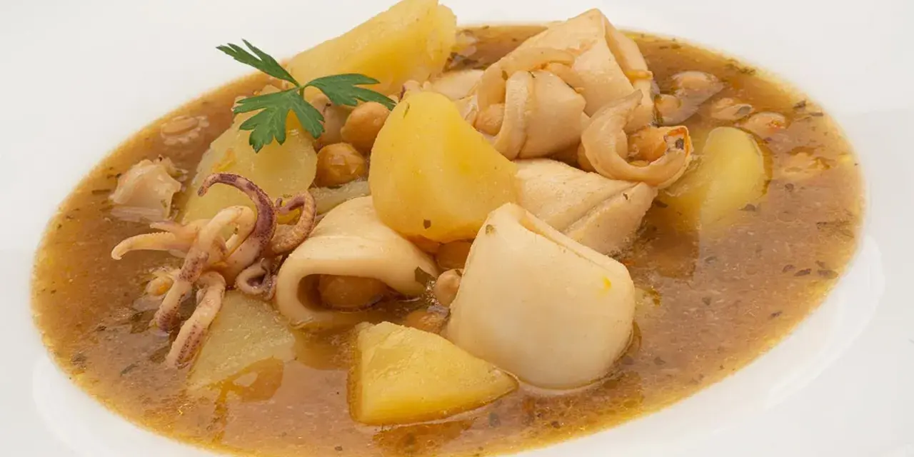 Guiso de garbanzos con trozos de calamar, patatas y perejil en un plato blanco.