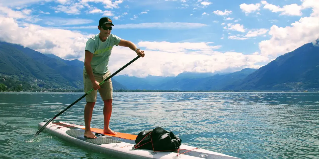 Mann auf SUP-Board mit Paddel, genießt die Geschwindigkeit auf dem See vor einer Bergkulisse.