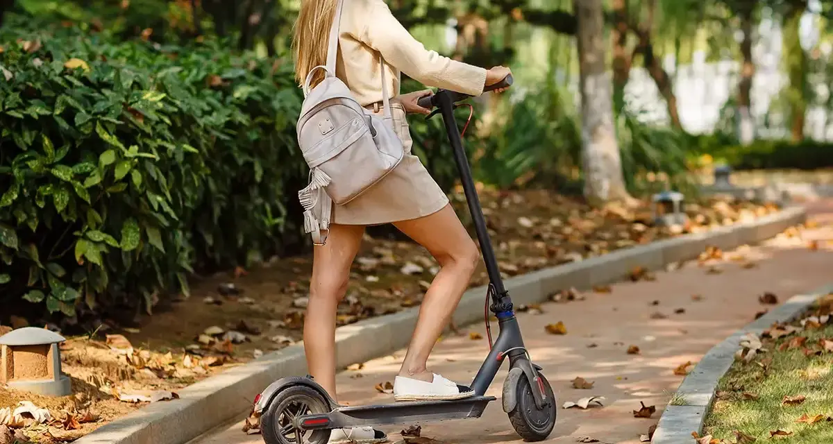 Ragazza su monopattino elettrico in un parco autunnale. Ricorda l'obbligo casco monopattino per la tua sicurezza.