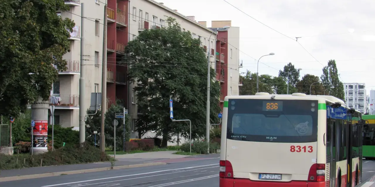 Autobus 8313 z numerem linii 836 czeka na przystanku. W tle budynki mieszkalne i drzewa.