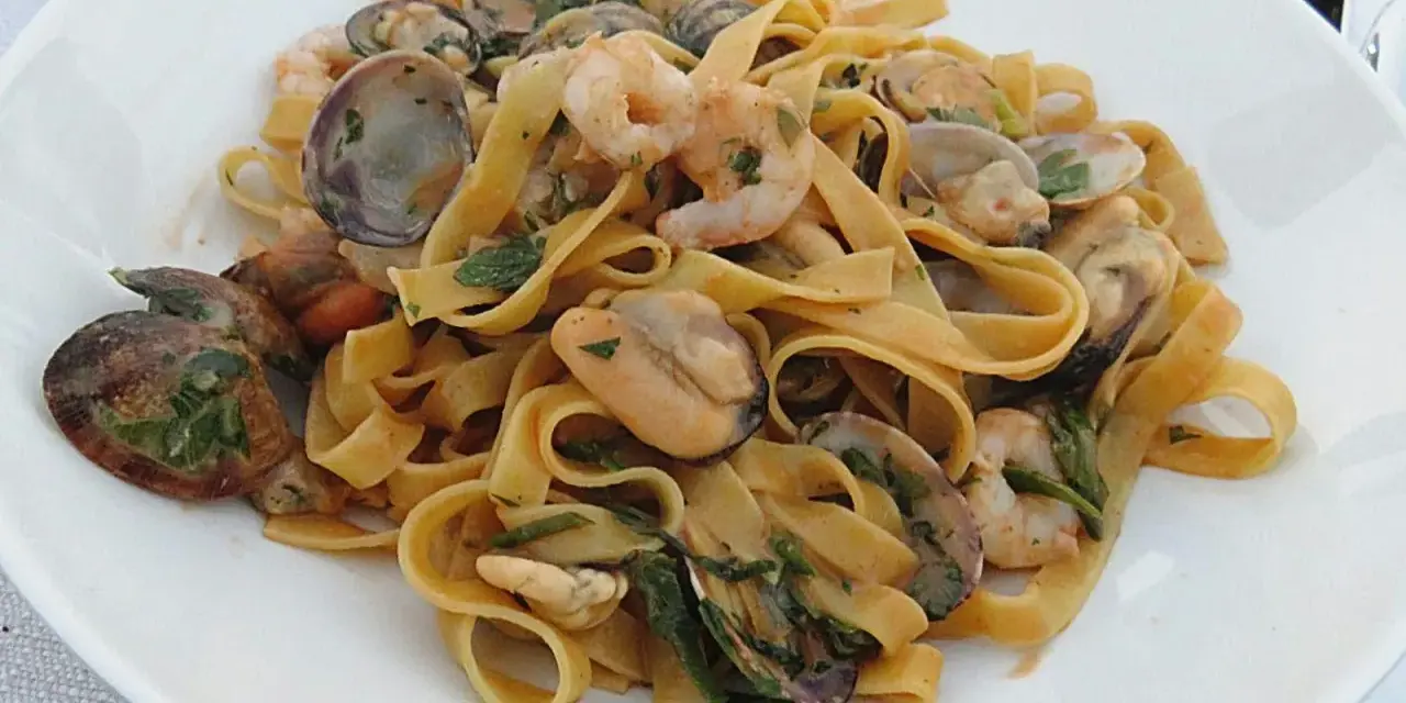 Un piatto invitante di tagliatella di mare con gamberi, cozze e vongole, condita con erbe fresche.