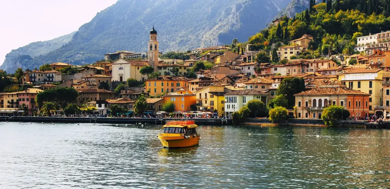 Un giallo battello solca il lago, dirigendosi verso il pittoresco borgo di Limone sul Garda, con le sue case colorate aggrappate alla montagna.