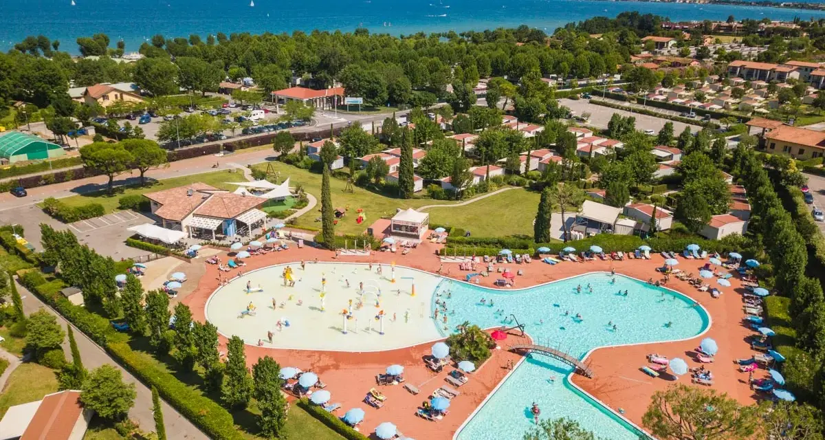 Widok z lotu ptaka na kompleks basenów i domków kempingowych w Sirmione. Woda lśni w słońcu, a ludzie cieszą się wakacjami na łonie natury.