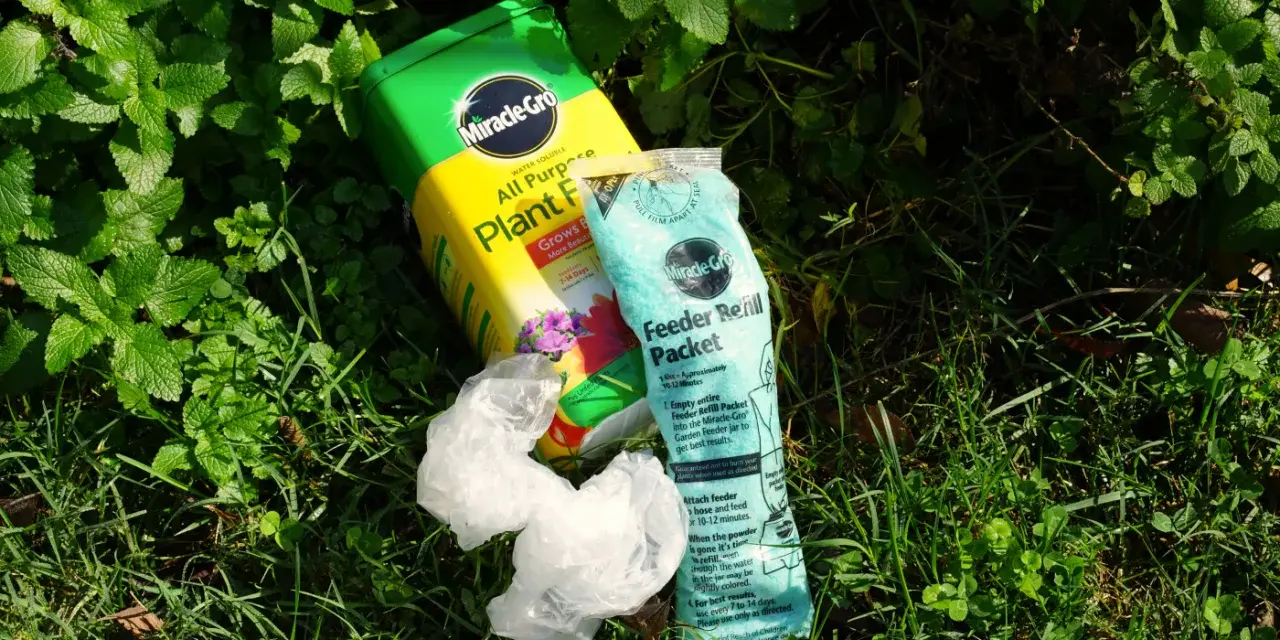 Miracle-Gro plant food and feeder refill packet lie on grass. While not inherently toxic, proper use is key to avoid harming plants.