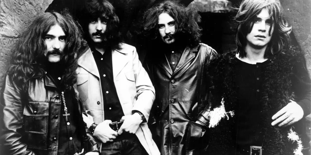 Członkowie zespołu Black Sabbath pozują do zdjęcia w mrocznym otoczeniu.