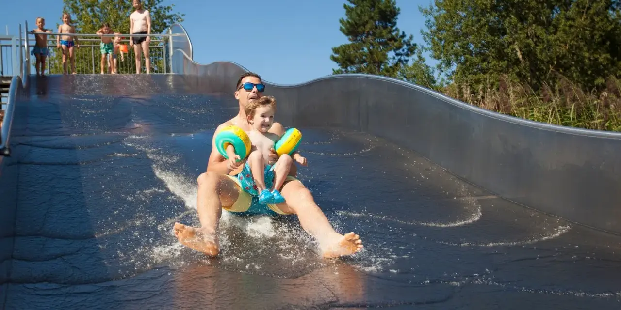 Vater und Sohn rutschen lachend die Wasserrutsche im Bostalsee Strandbad hinunter.