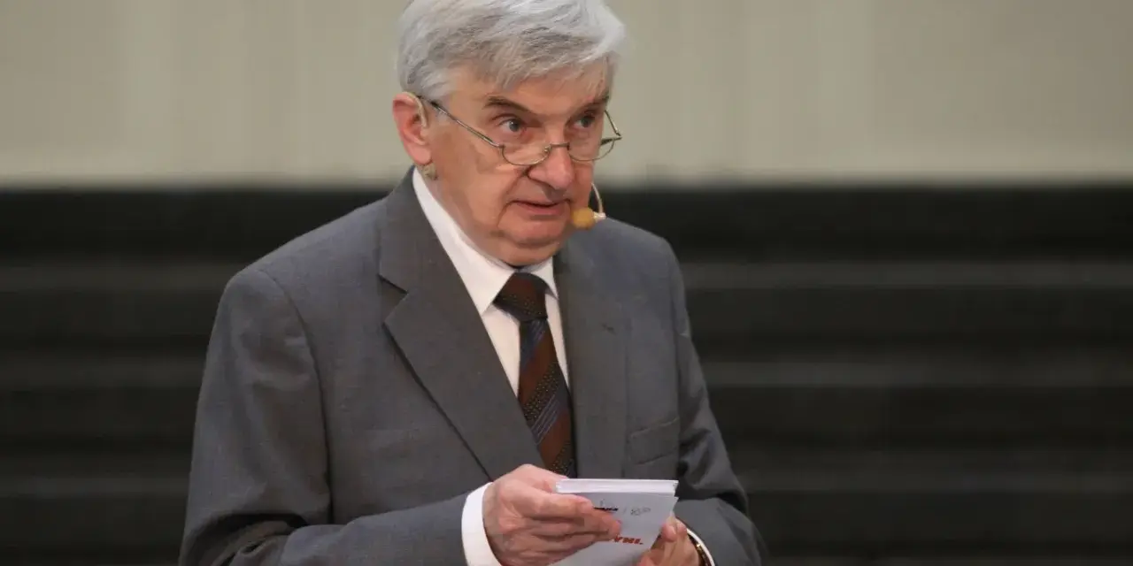 Starszy mężczyzna w garniturze, który prowadzi jeden z dziesięciu, trzyma kartkę.