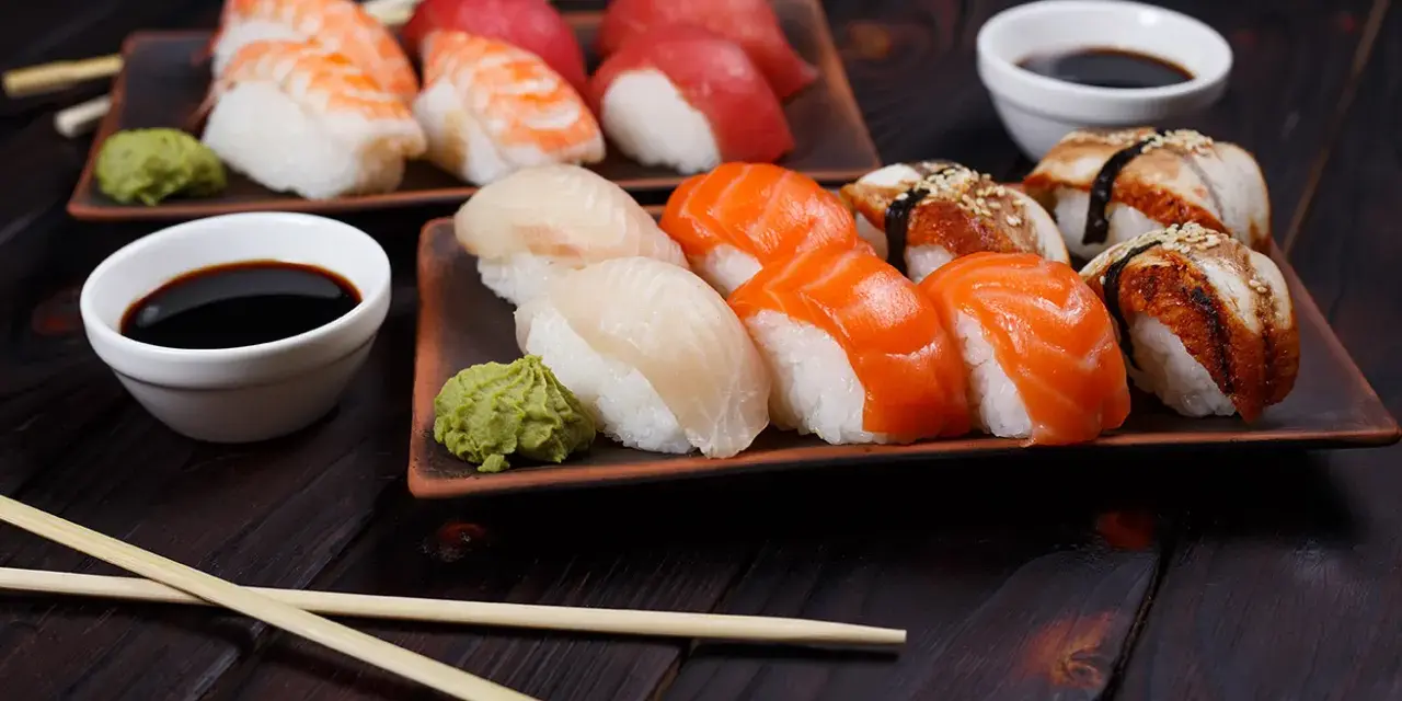 Różnorodne rodzaje sushi: nigiri z krewetką, łososiem, białym rybą i węgorzem, podane z wasabi i sosem sojowym.