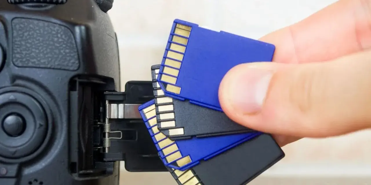Main tenant, une main s'apprête à insérer une carte SD dans un appareil photo. Il est temps de choisir la carte SD parfaite pour vos souvenirs.