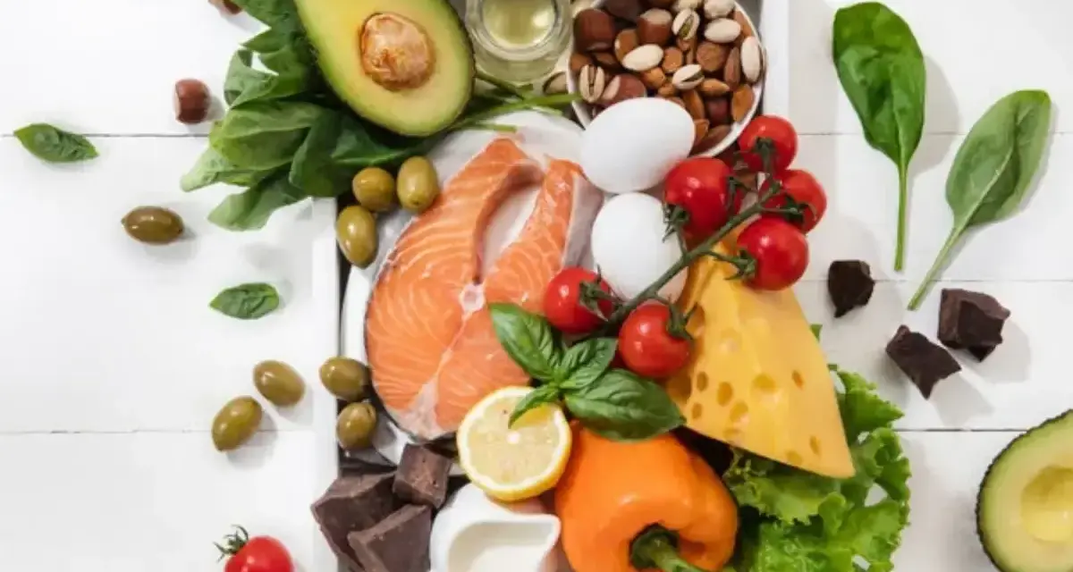 Składniki na dieta keto jadłospis: łosoś, awokado, jajka, ser, orzechy, oliwki, warzywa i gorzka czekolada.