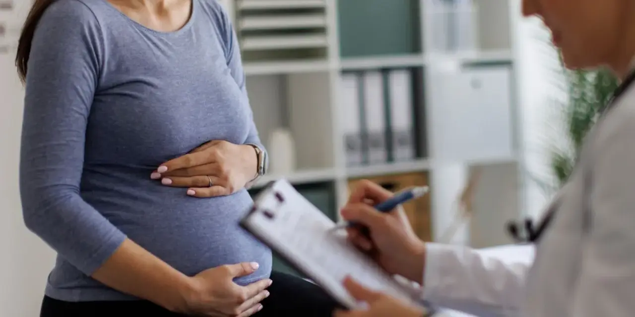 Visita medica: una donna incinta tiene la pancia mentre il medico annota sul foglio, forse il tracciato delle contrazioni preparatorie.