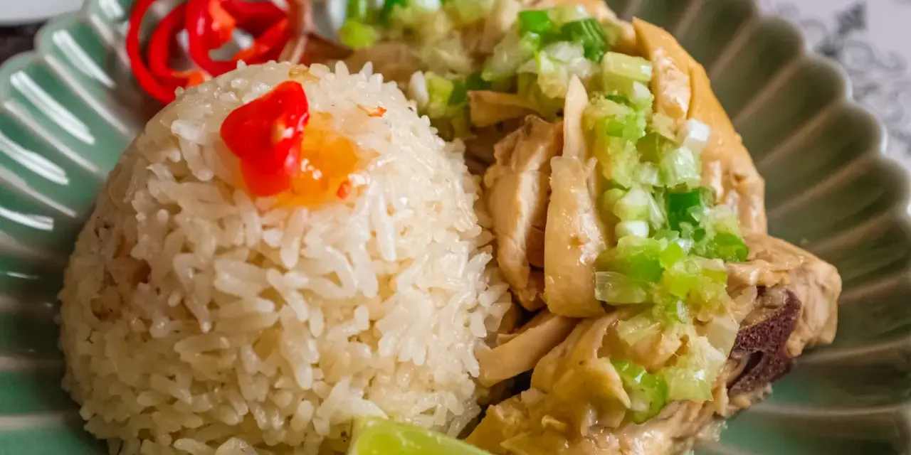 Un invitante piatto di riso con pollo, guarnito con cipollotti freschi, peperoncino rosso e una fetta di lime.