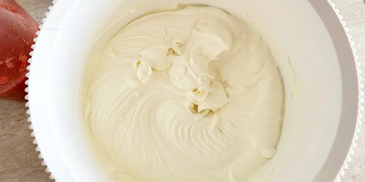 Gładki, puszysty **prosty krem z mascarpone bez śmietany** w białej misie, gotowy do deseru. Obok miski widać miseczkę z truskawkami.