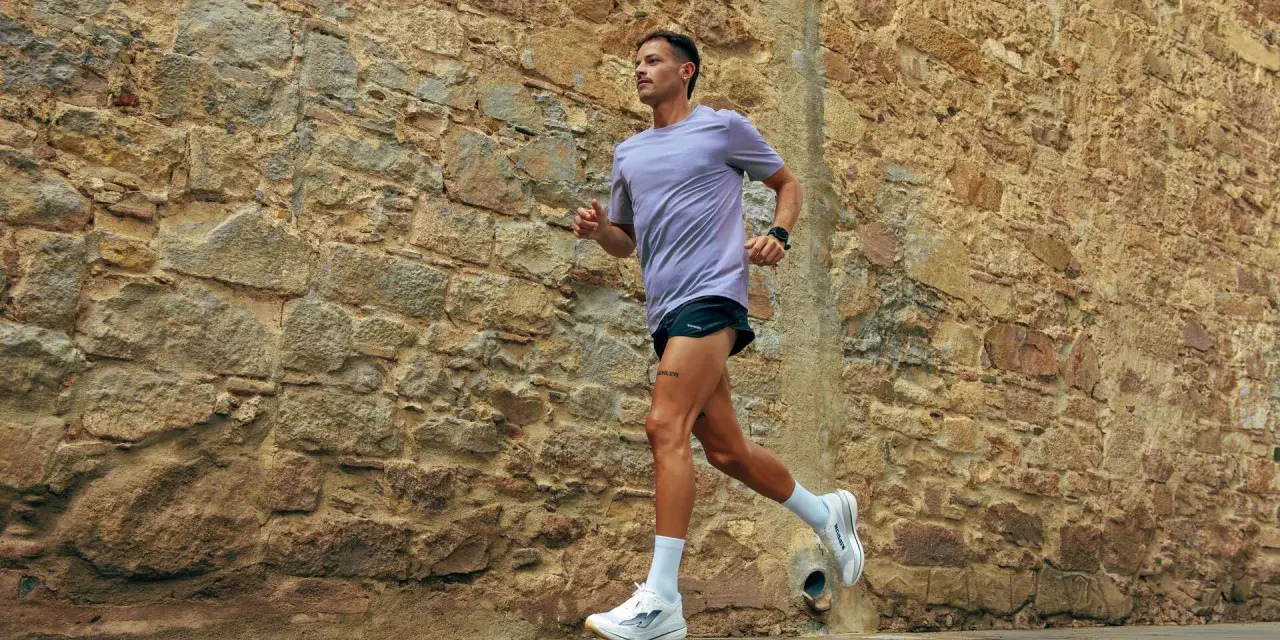 Uomo con tatuaggio corre lungo un muro di pietra. La sua tecnica di pronatore corsa è fluida e potente.
