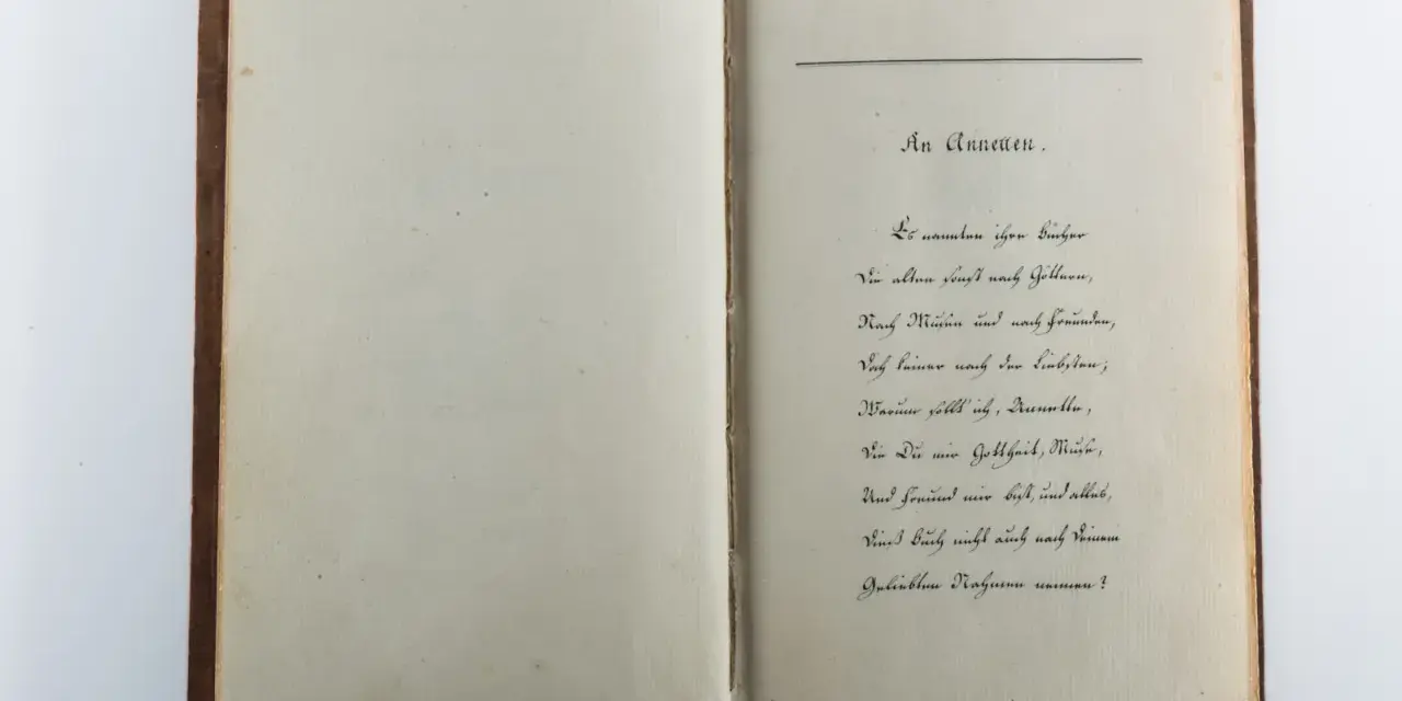 Ein aufgeschlagenes Buch mit handschriftlichem Gedicht auf der rechten Seite.