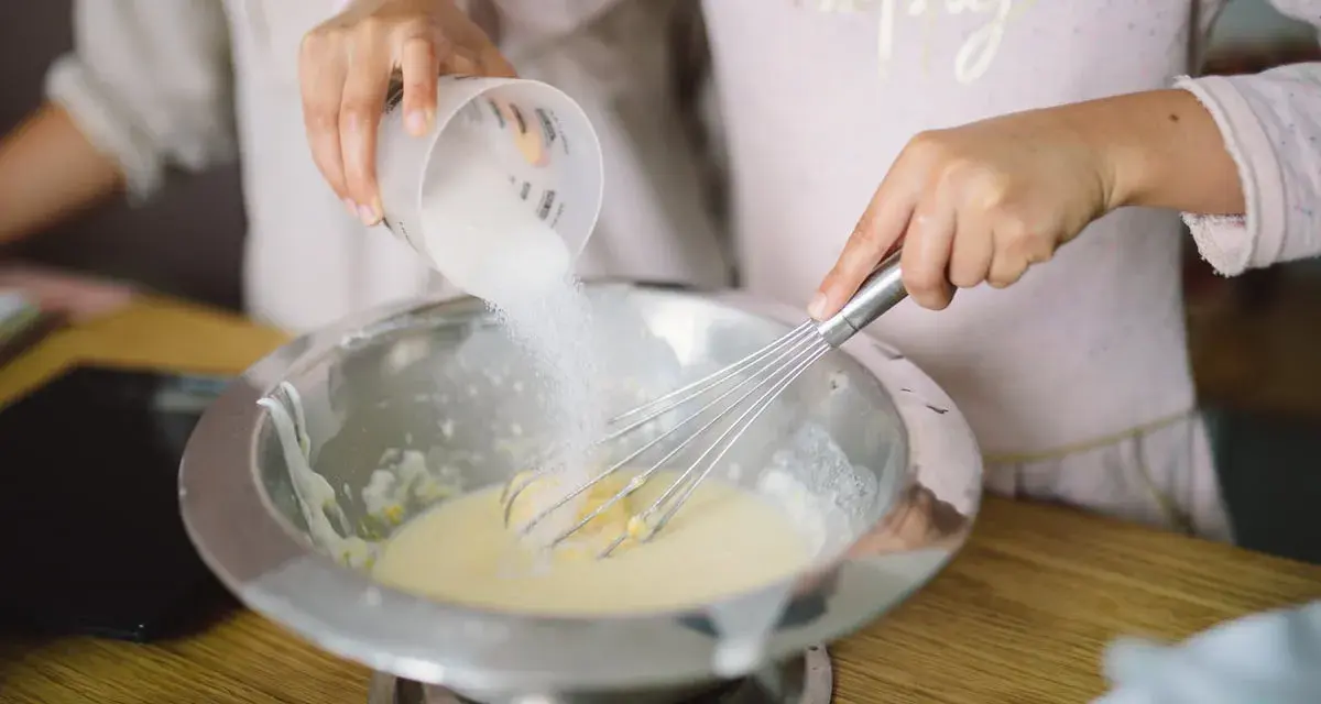 Préparation de la pâte à crêpes : on ajoute du sucre dans le bol avec un fouet. C'est la base de la recette des crêpes.