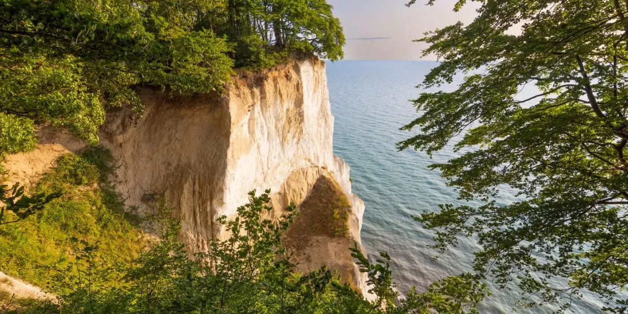 Weiße Kreidefelsen ragen steil aus dem ruhigen Meer der Ostsee. Grüne Bäume säumen die Klippen und bieten einen friedlichen Ausblick.