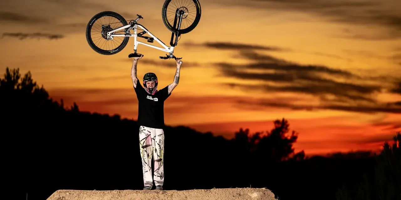 Tomas Lemoine triumphantly raises his bike against a fiery sunset, a champion on the dirt jump.