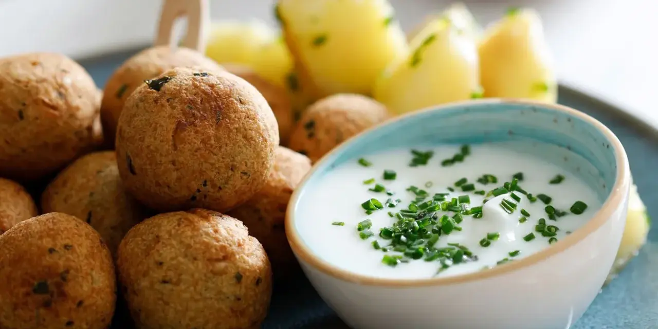 Polpette di ceci dorate e croccanti, servite con patate novelle e una ciotola di salsa cremosa guarnita con erba cipollina.