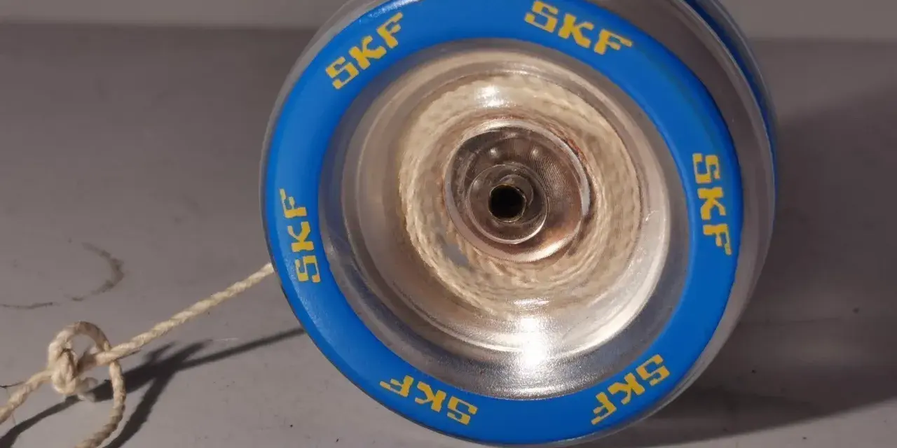 Blå jojo med kullager och texten "SKF" runt kanten. Snöret är knutet och ligger på ett grått underlag.