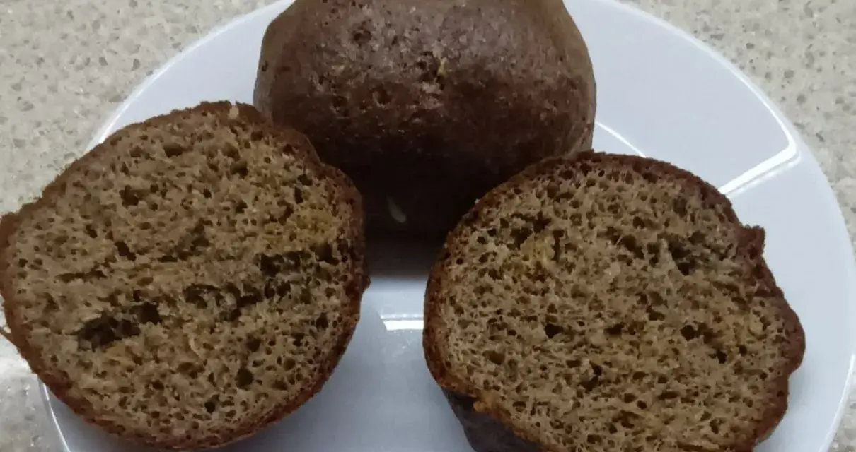 Na talerzu leżą keto bułki babka jajowata. Jedna jest cała, dwie pozostałe przekrojone na pół, ukazując puszyste wnętrze.