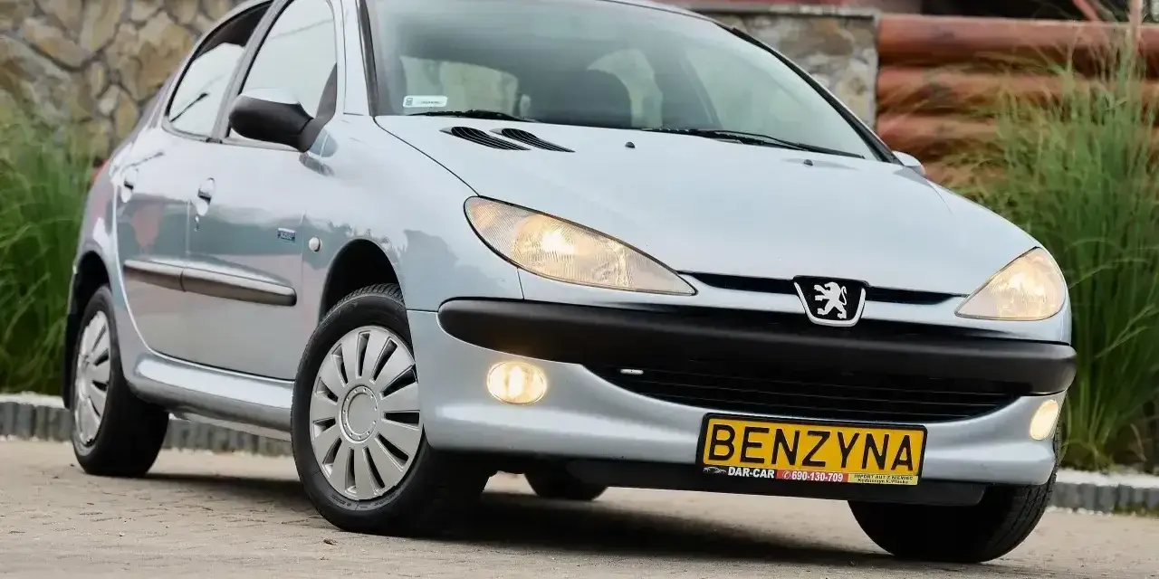 Jasny Peugeot 206 1.4 benzyna z żółtą tablicą "BENZYNA" na zderzaku, zaparkowany na zewnątrz.