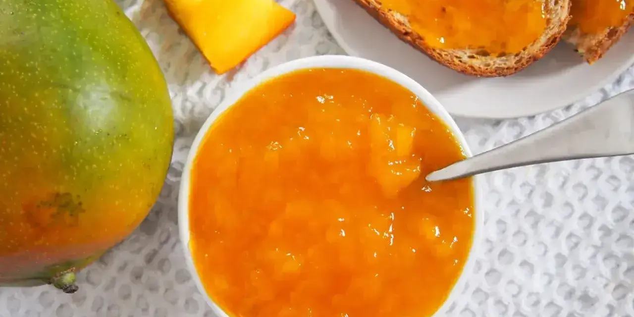 Słoik z dżemem z mango, obok świeży owoc i kromki chleba. Codzienne jedzenie mango to pyszny początek dnia.