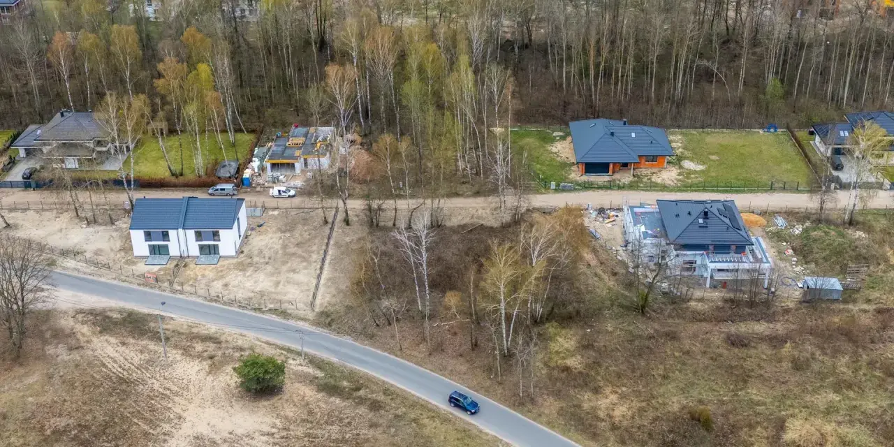 Widok z lotu ptaka na budowę domów jednorodzinnych, tworzących nowy plan ogólny gminy. Widać domy w różnym stanie budowy i drogę.
