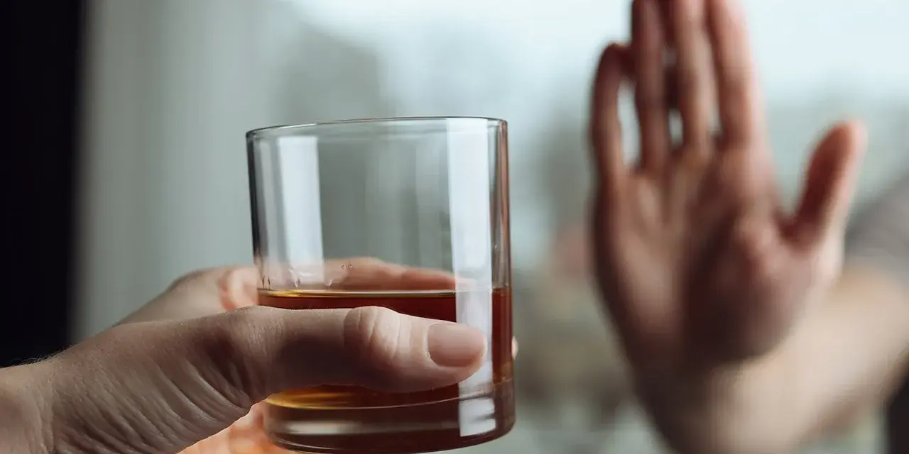 Dłoń odrzuca szklankę z alkoholem, symbolizując koniec z nałogiem i wyciek z wszywki.