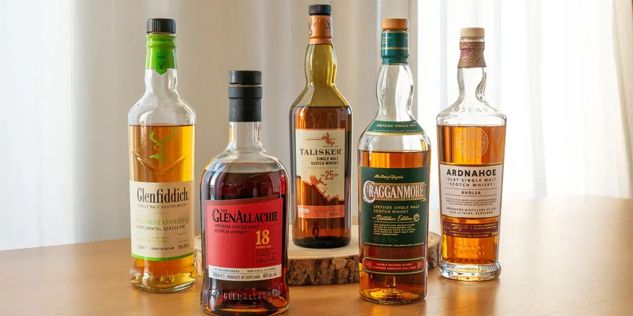 Fünf Flaschen gute Whiskey-Sorten: Glenfiddich, Glenallachie, Talisker, Cragganmore und Ardnahoe stehen auf einem Holztisch.