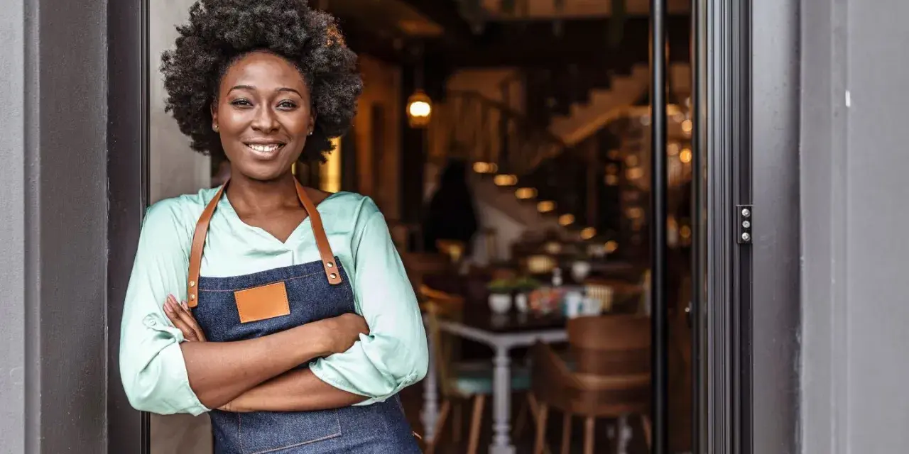 Mujer sonriente con delantal, lista para abrir su restaurante. Su plan de negocio es sólido.