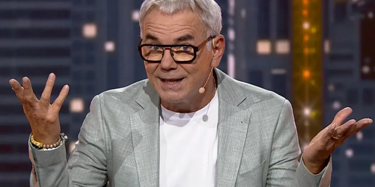 Mężczyzna w okularach, w jasnej marynarce, gestykuluje. Może to być kadr z programu "Jaka to melodia" (wikipedia).
