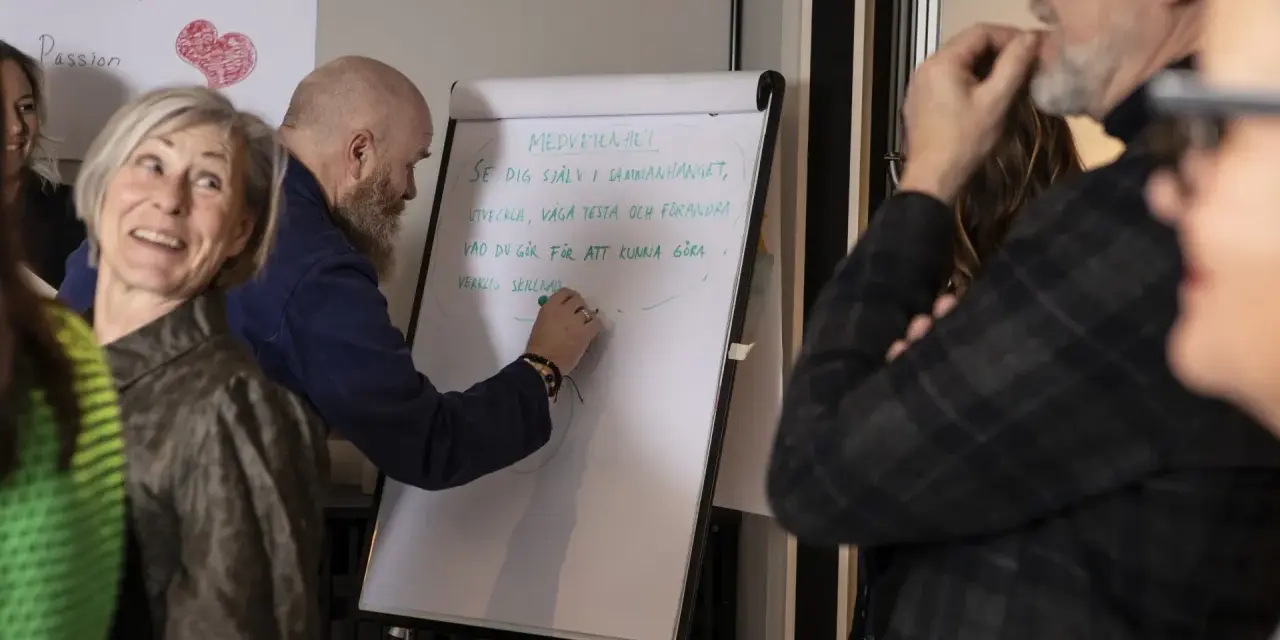 En grupp människor diskuterar hur en bra chef ska vara. En man skriver på en whiteboard om medvetenhet och utveckling.