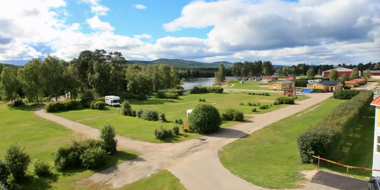 Vacker vy över svegs camping med husbilar, stugor och en sjö i bakgrunden under en molnig himmel.