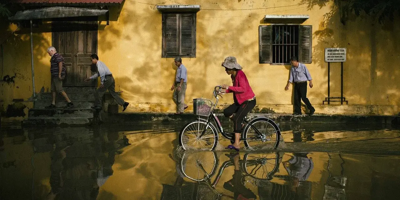 Une femme à vélo traverse une rue inondée, reflétant la vie quotidienne. Quel objectif pour photo de rue capture cette scène ?