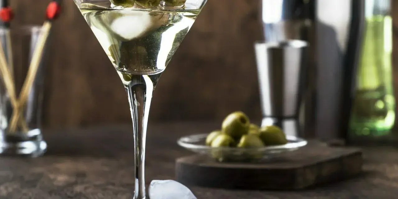 Elegancki martini z oliwką, gotowy do degustacji. Obok kostki lodu i talerzyk z oliwkami.
