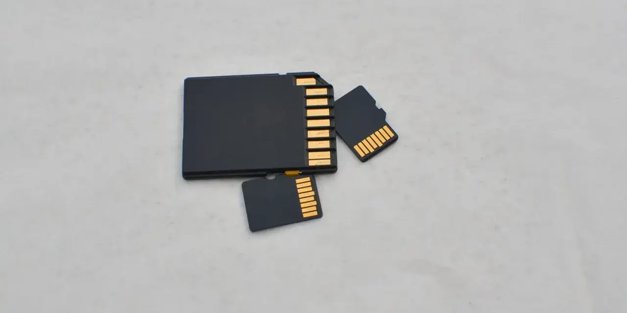 Trzy czarne karty pamięci: jedna większa, przypominająca kartę SD, oraz dwie mniejsze, typu microSD. Złote styki widoczne na każdej karcie.