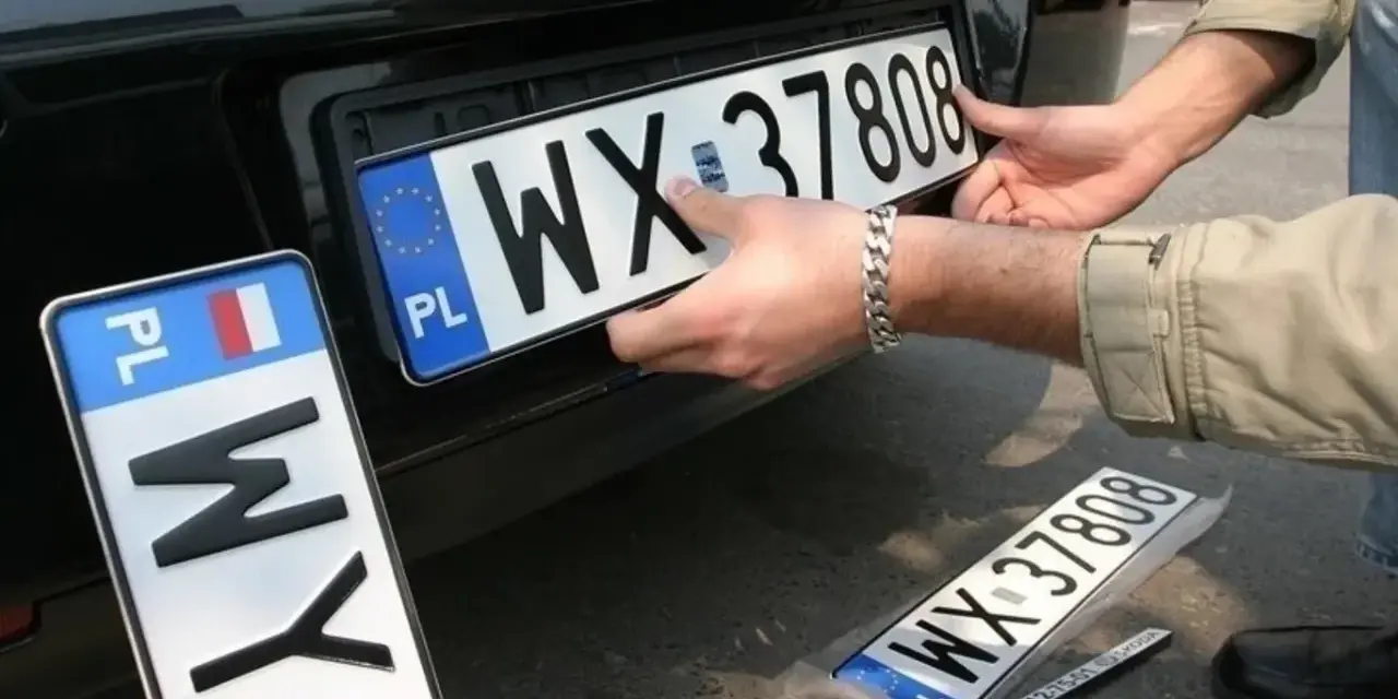 Montaż nowych tablic rejestracyjnych. Jedna z nich, z numerem WX 37808, jest właśnie wkładana. Obok leży kolejna, jeszcze w folii.