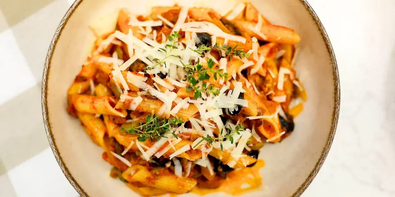 Penne z bogatym sosem anchois, czarnymi oliwkami i parmezanem, udekorowane świeżym tymiankiem.
